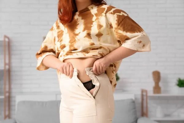 Image of woman trying to do her trousers up after pregnancy weight gain Harpenden